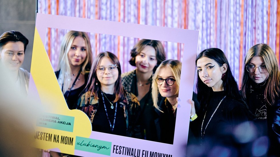Grupa młodych osób pozuje do zdjęcia z ramką promocyjną Festiwalu Kamera Akcja