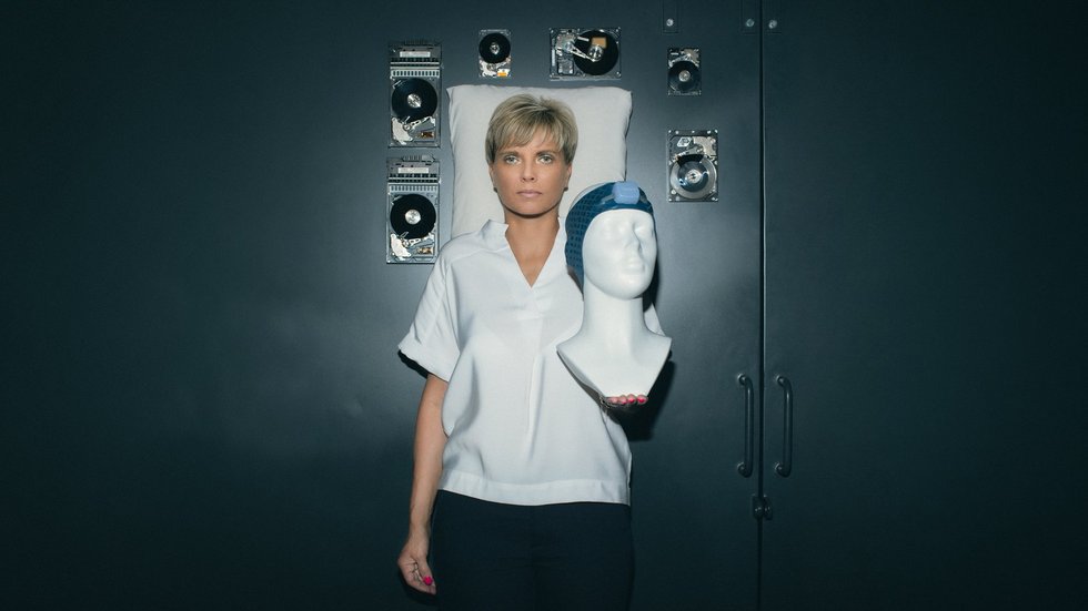 Prof. Renata Bocian trzymająca manekina z opaską Vguard w tle poduszka oraz unoszące się w przestrzeni twarde dyski komputerowe