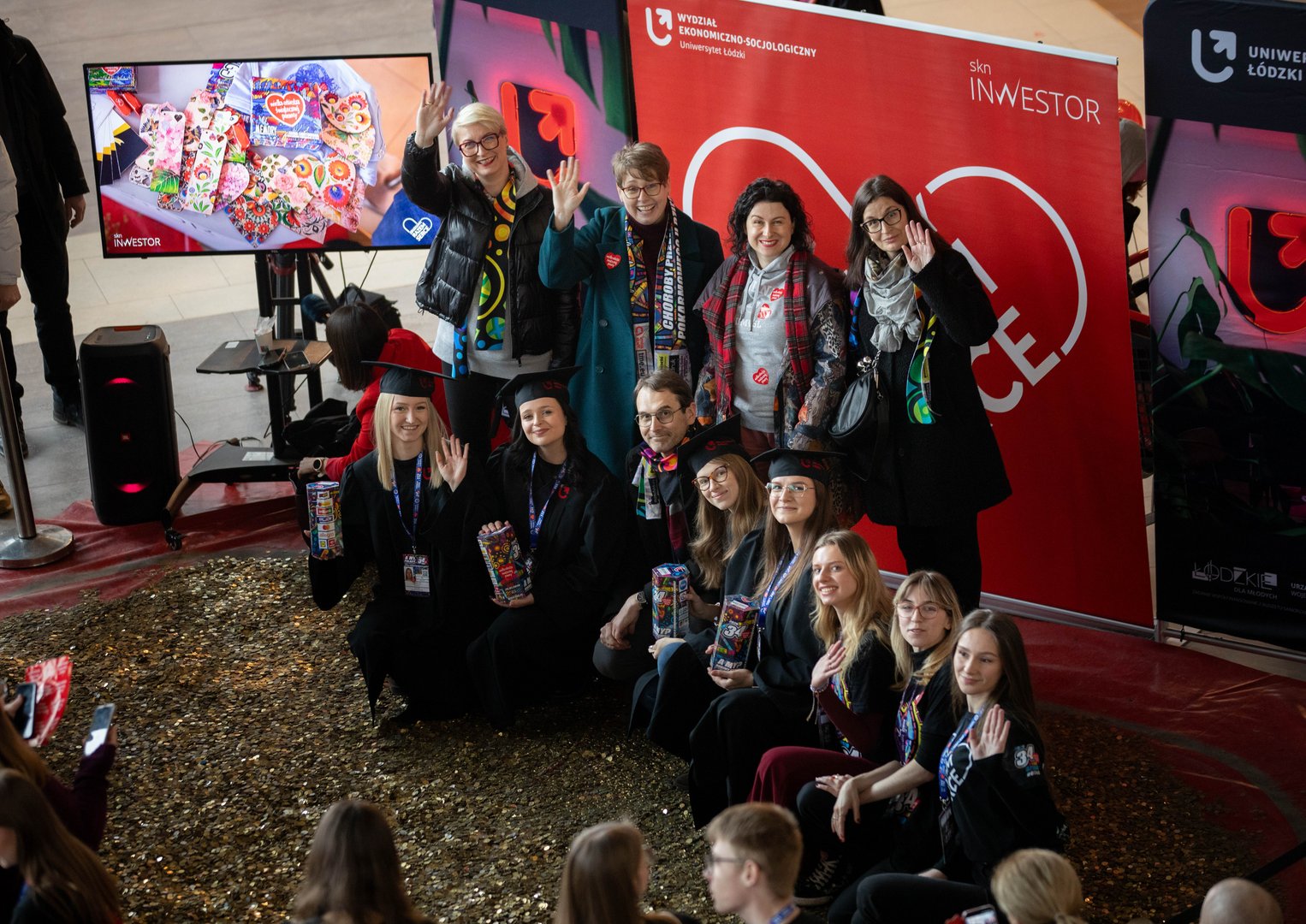 Grupa osób - Przedstawicielki Władz UŁ i studentki UŁ stojace na wielkim sercu wypełnionym złotymi monetami