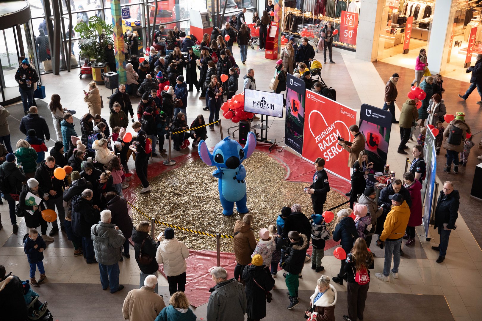 Widok z góry na ludzi stojących wokół wielkiego serca składającego się ze złotych monet